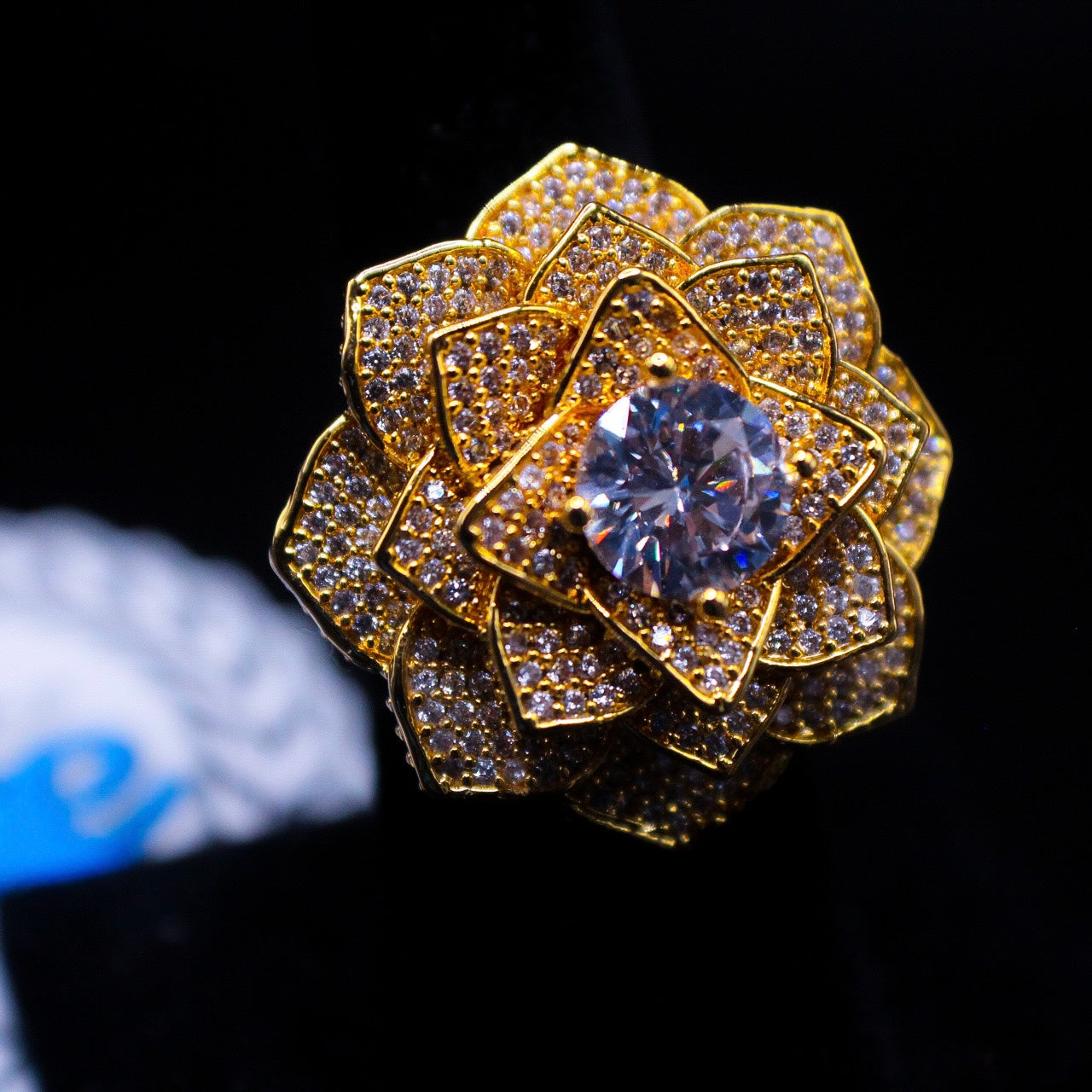 A yellow gold ring with a 3D rose design, featuring a central cubic zirconia surrounded by smaller clear crystals set in a textured gold band.