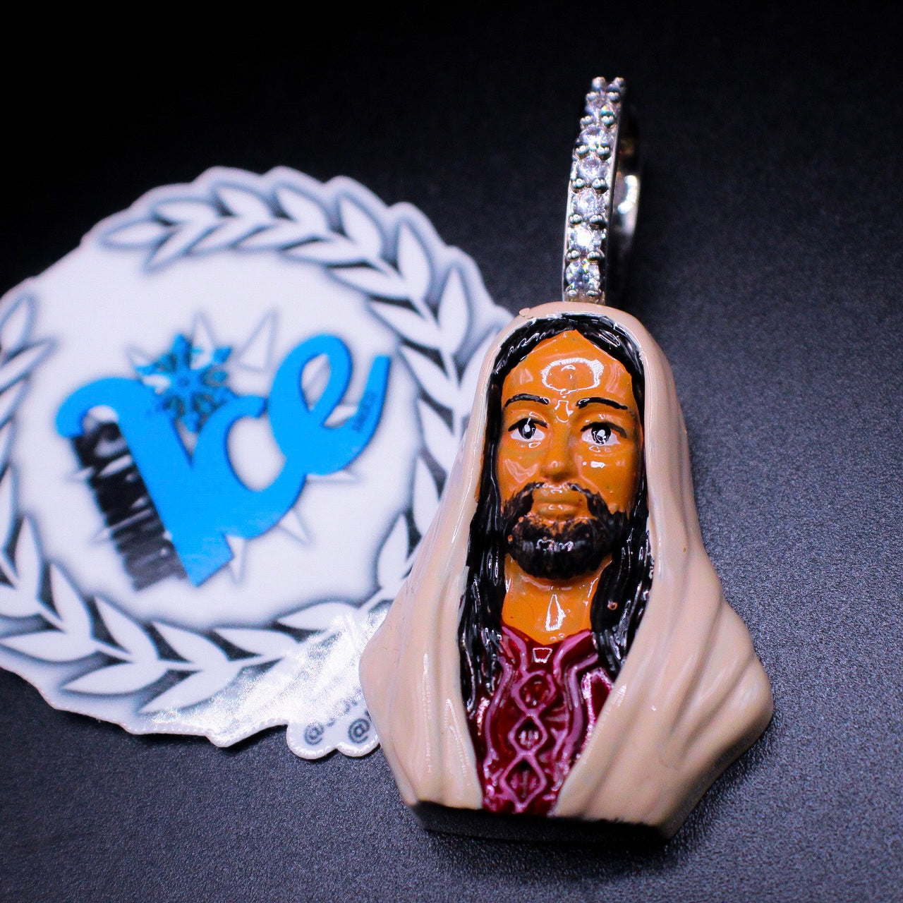 An enamel charm depicting a stylized Jesus figure, with a silver finish and a label with 'ICE' branding in the background.