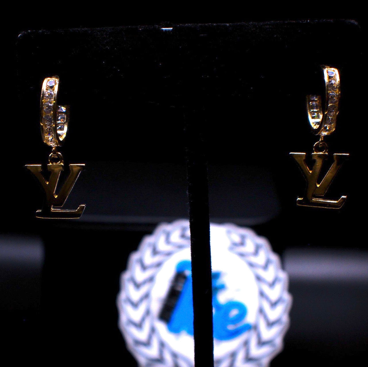 Gold earrings with 'LV' logo on a black stand