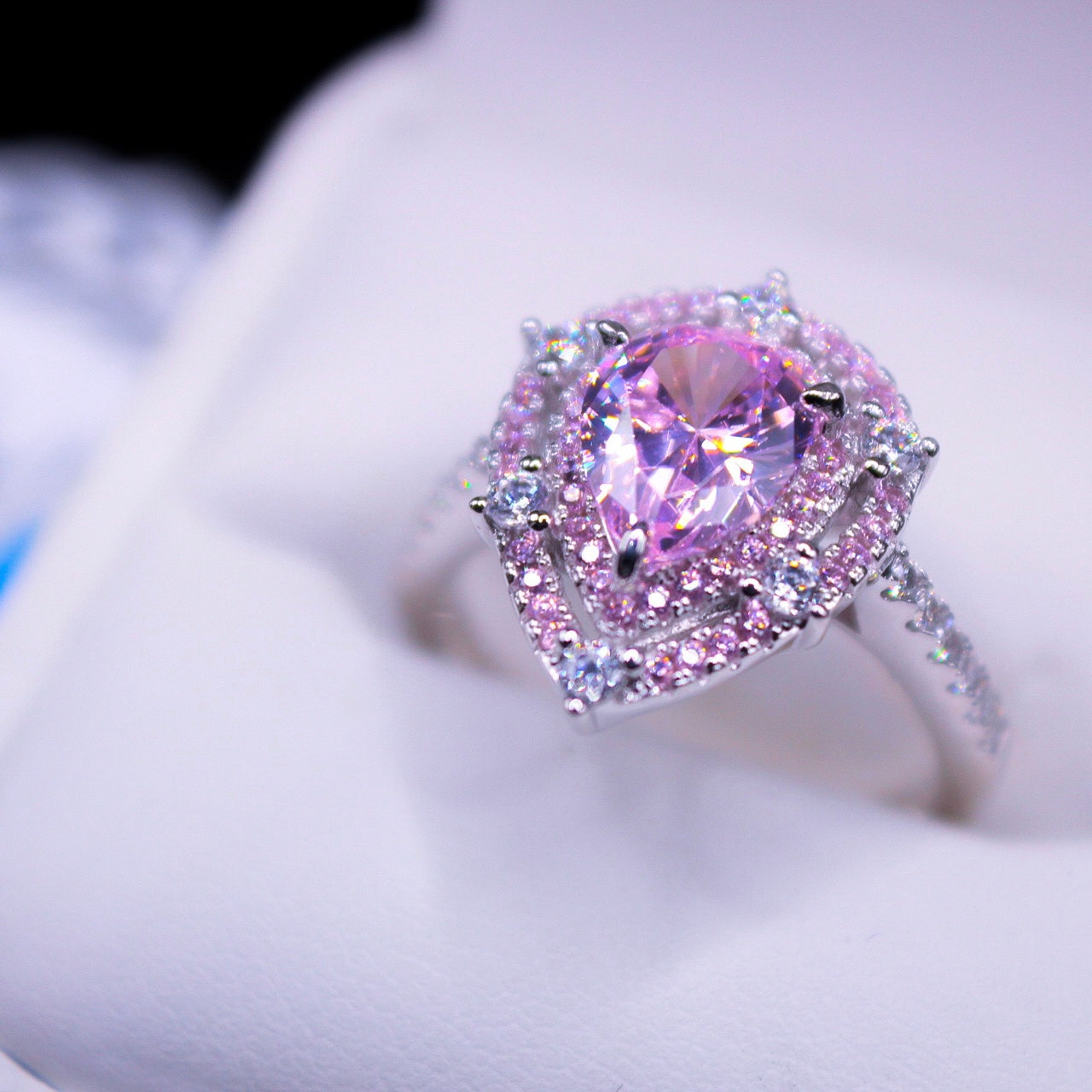 A teardrop-shaped pink gemstone ring with a triple row of smaller stones set in a silver band, displayed against a white background.