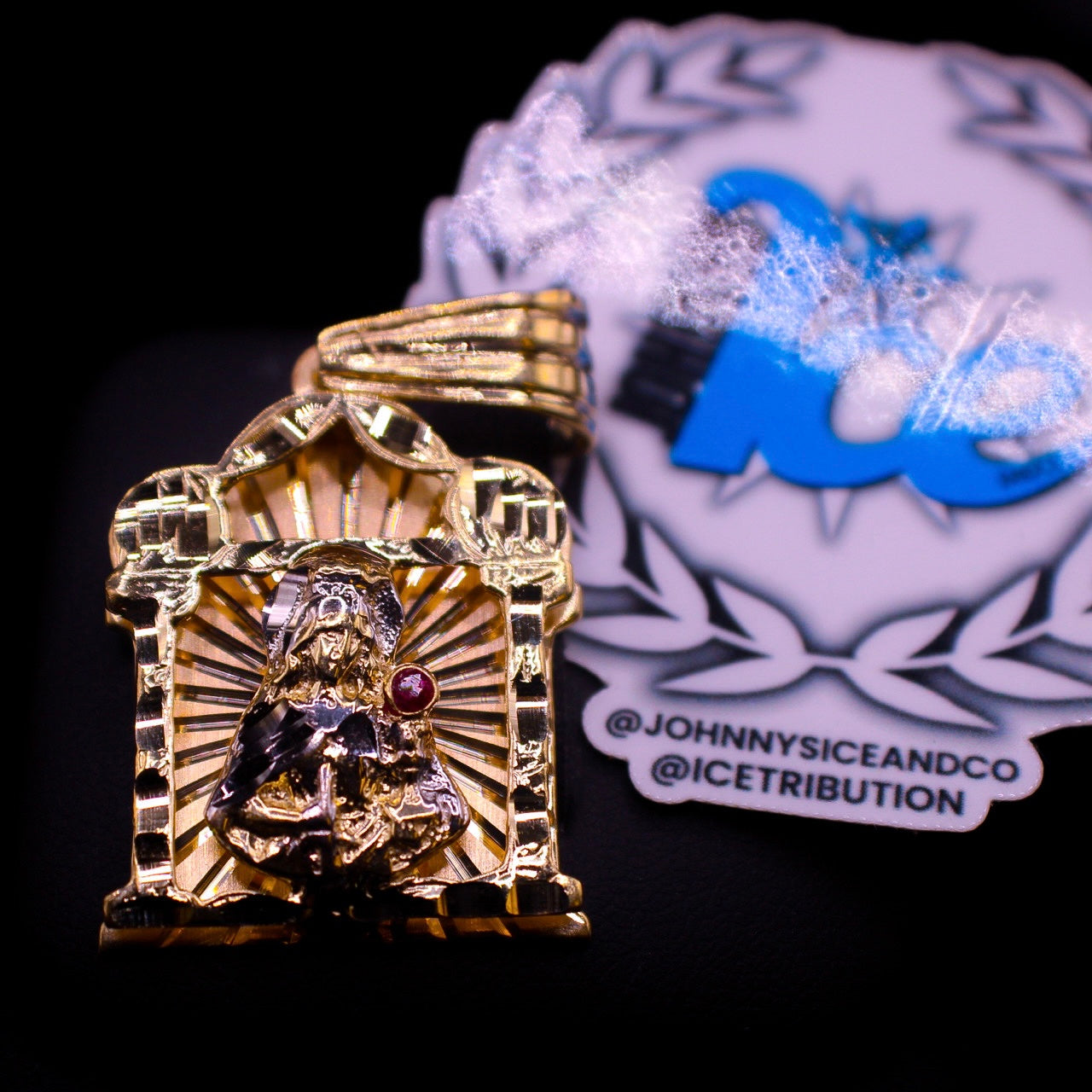 A gold pendant featuring a red ruby piece with intricate engravings, displayed against a branded background.