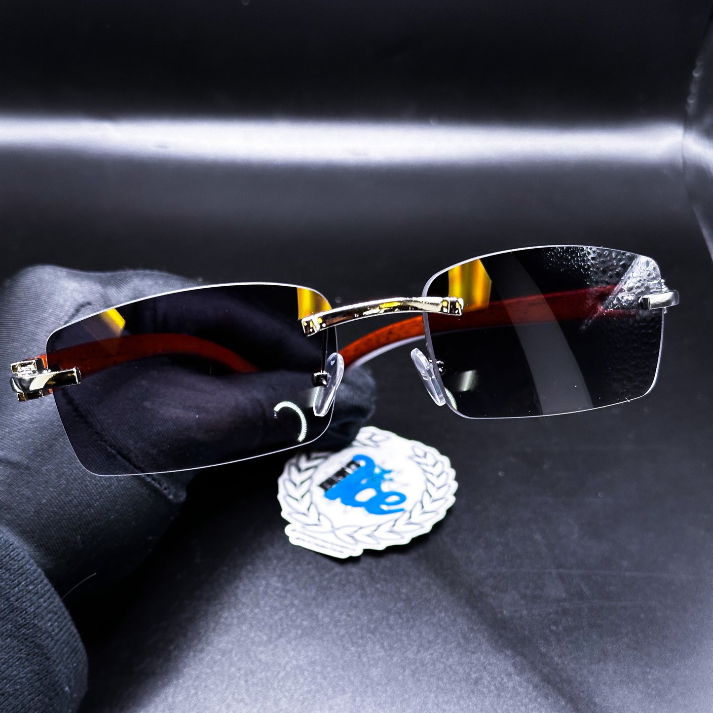 A pair of black sunglasses with a metallic frame, displayed on a dark surface alongside a blue and white branded cloth.