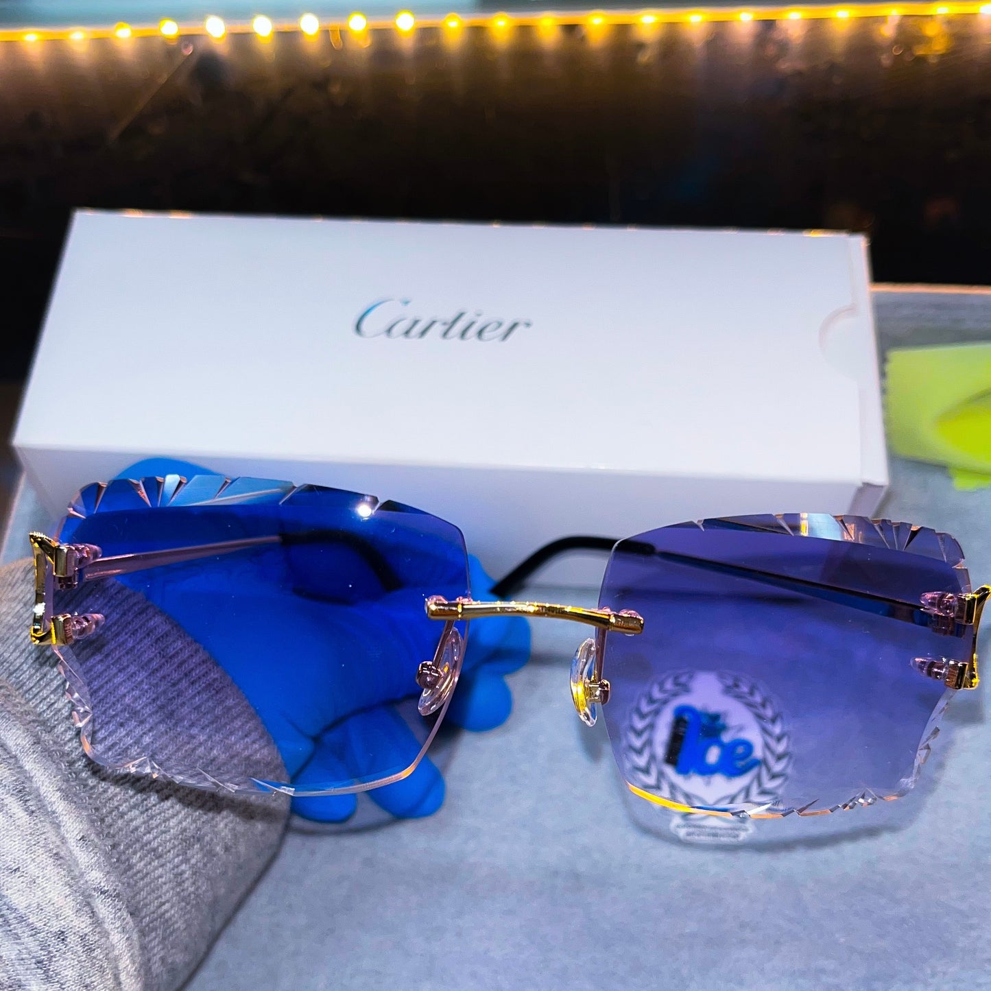 A pair of rimless, purple sunglasses with custom cut lenses, displayed in front of a Cartier box.