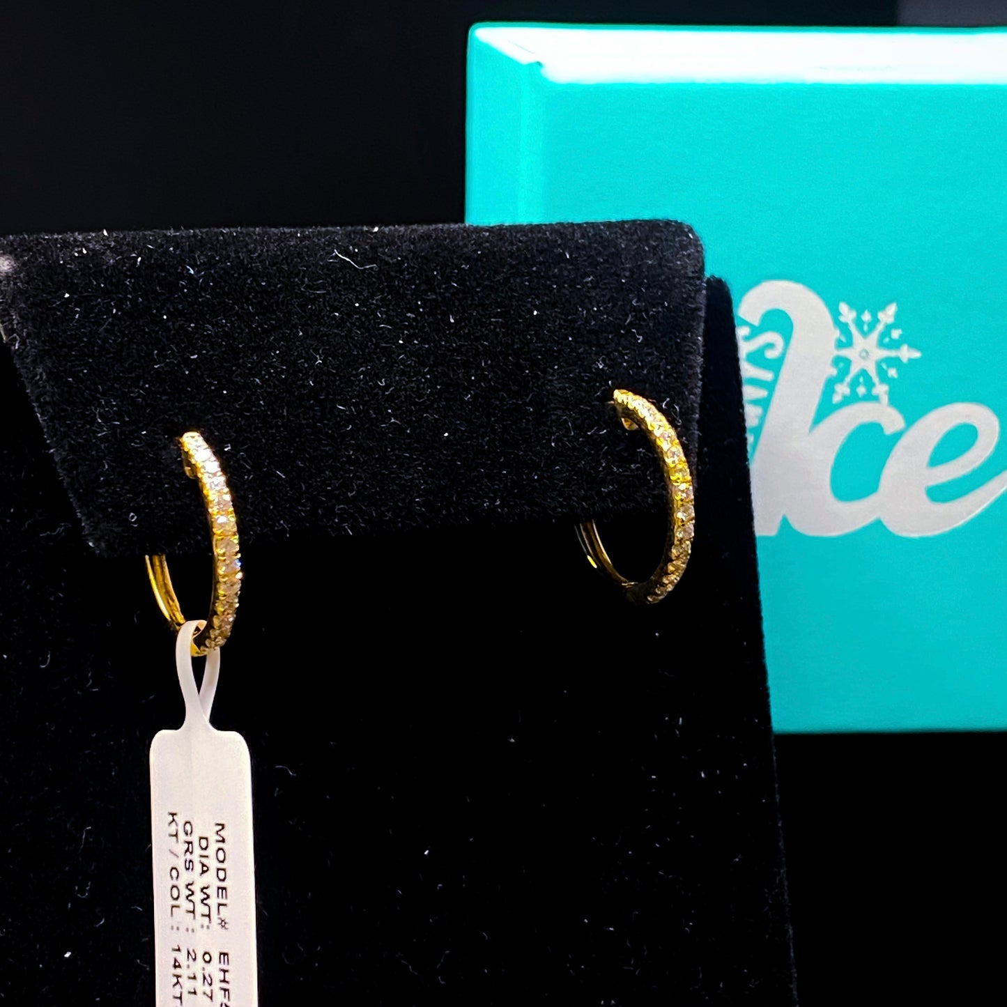 Gold hoop earrings on a black stand with a turquoise box in the background