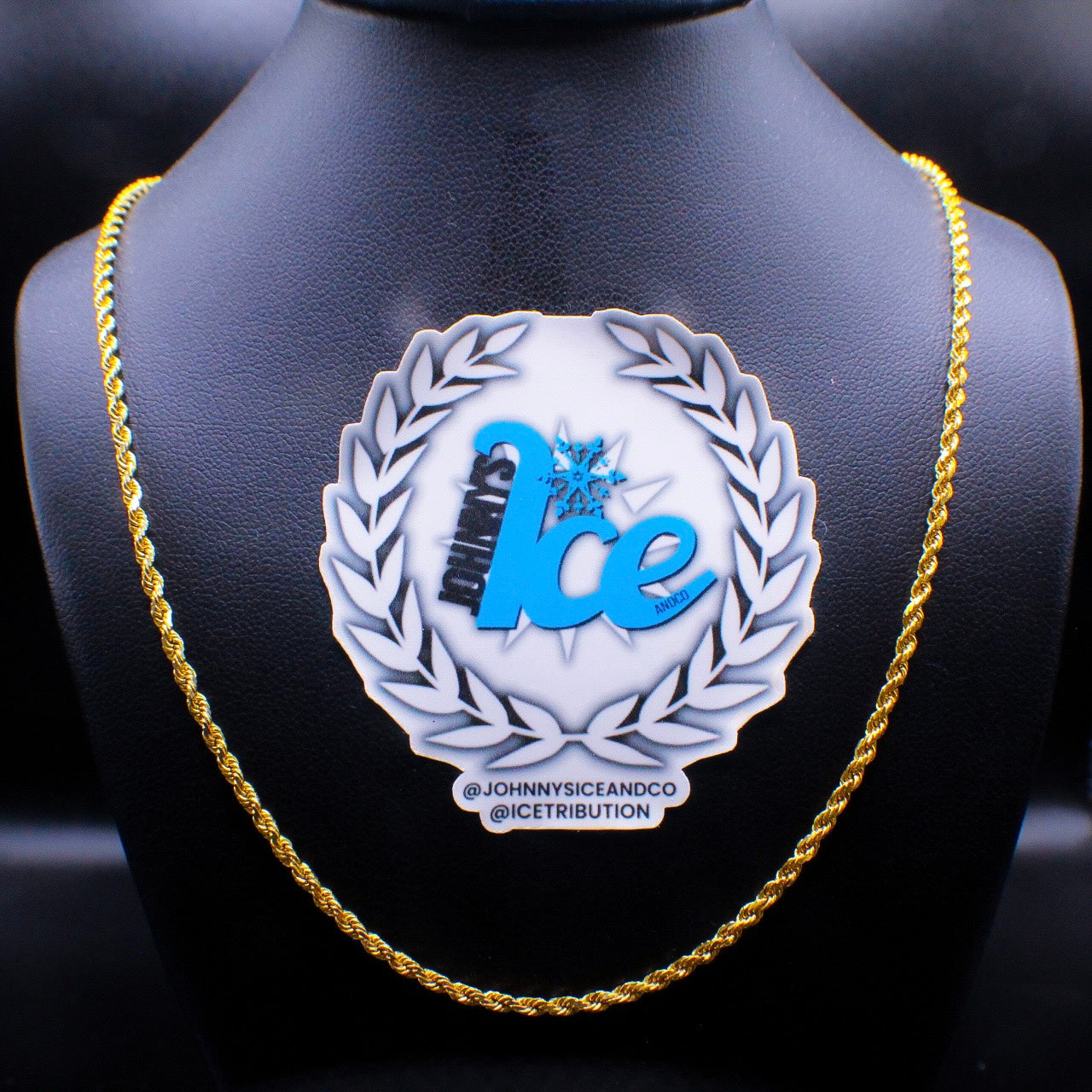 A gold rope chain necklace displayed on a mannequin torso with a branded display stand in the background.