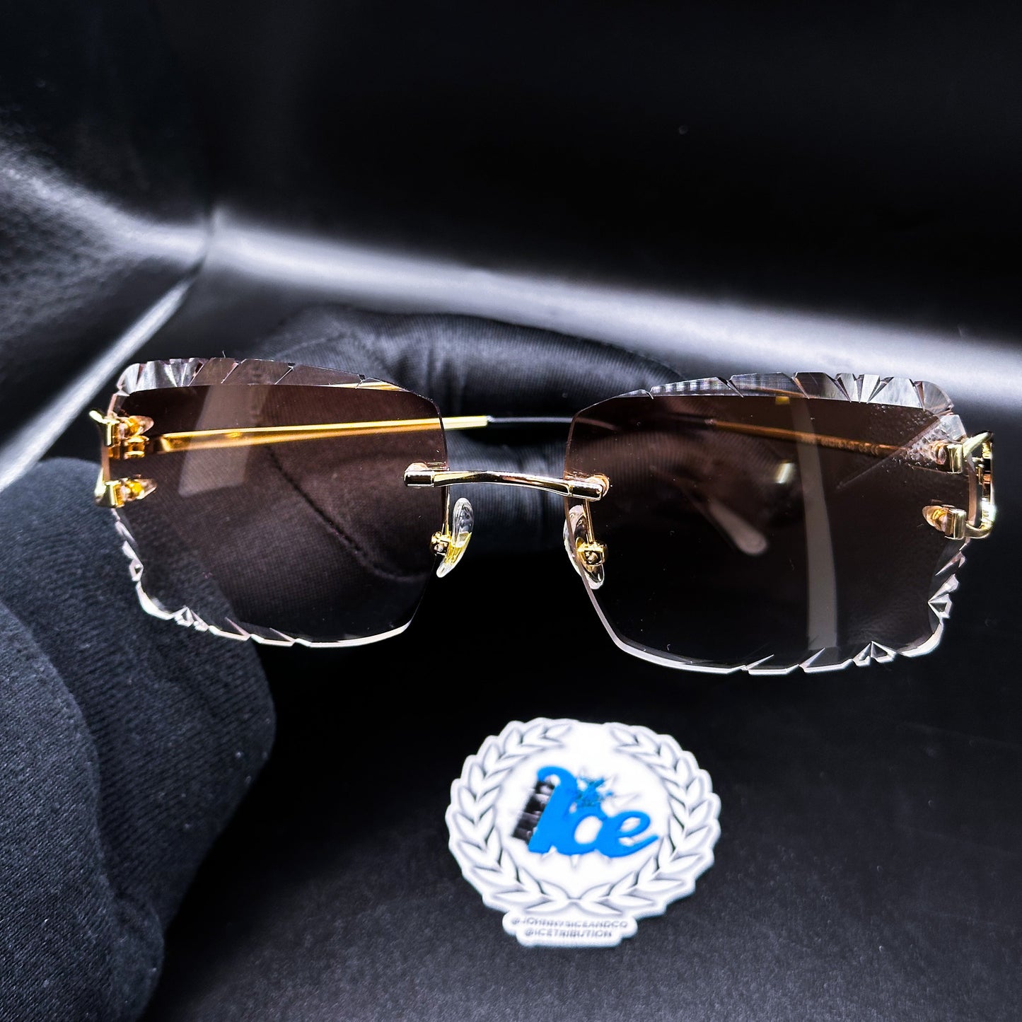 A pair of elegant brown wire-framed sunglasses displayed against a dark background, with a custom cut brown lens and a visible brand logo.