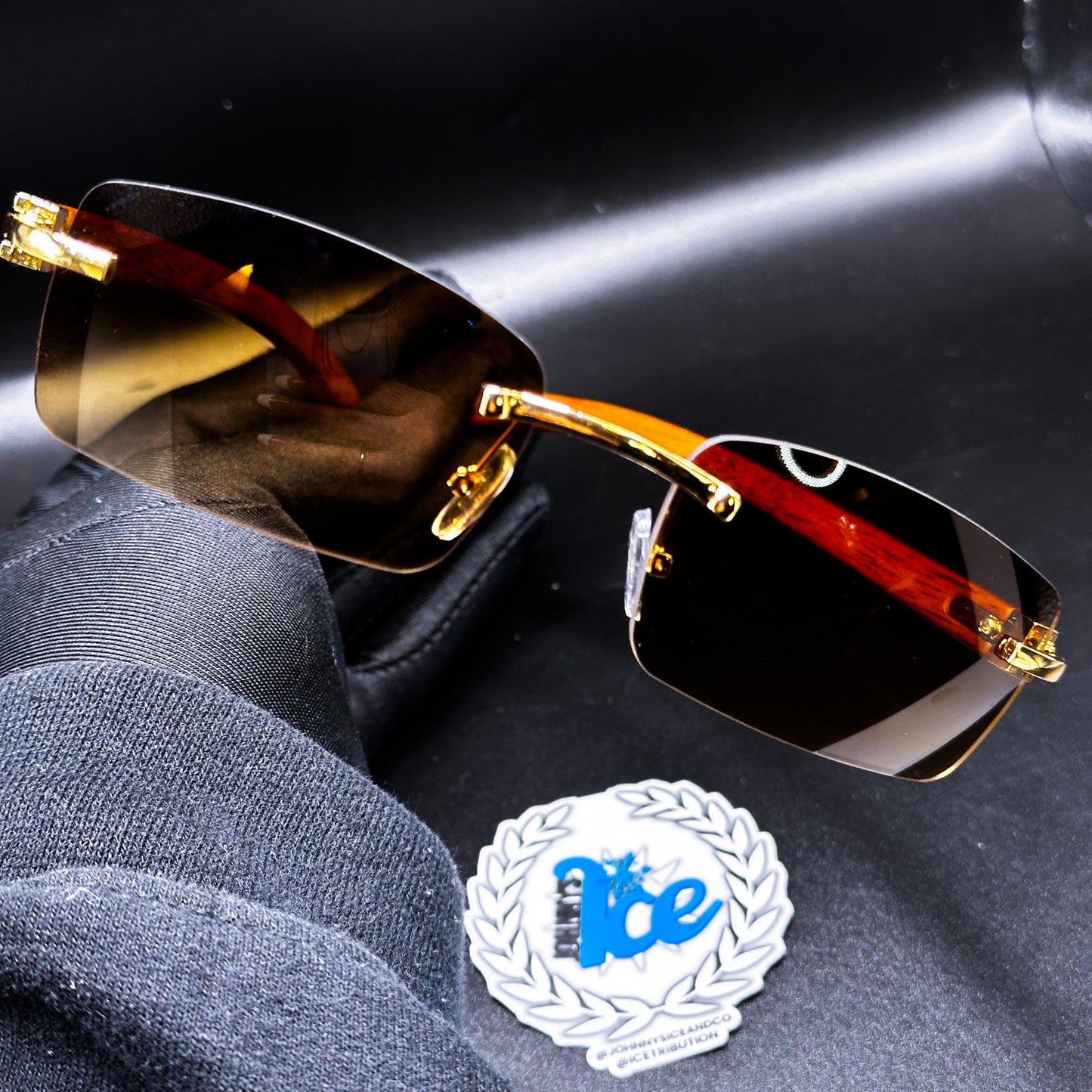 A pair of sunglasses with golden brown lenses and a brown metallic frame, displayed on a dark surface next to a coin.