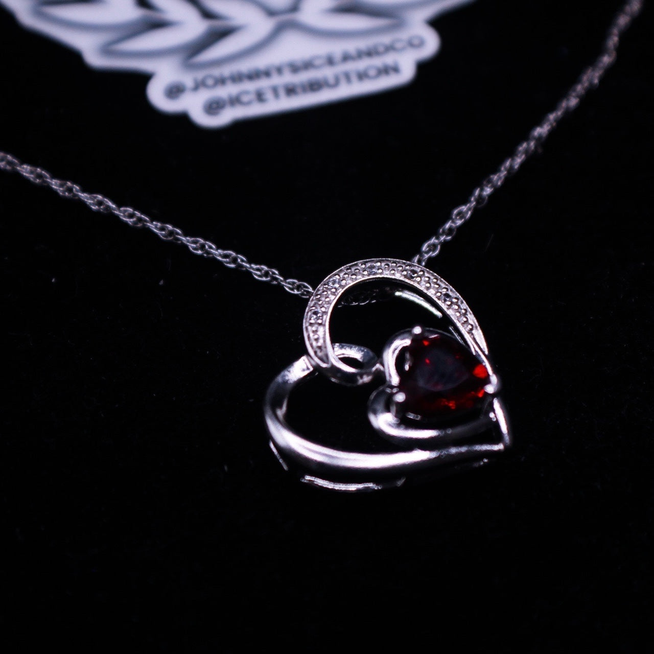 Heart-shaped silver pendant with a red gemstone on a black background