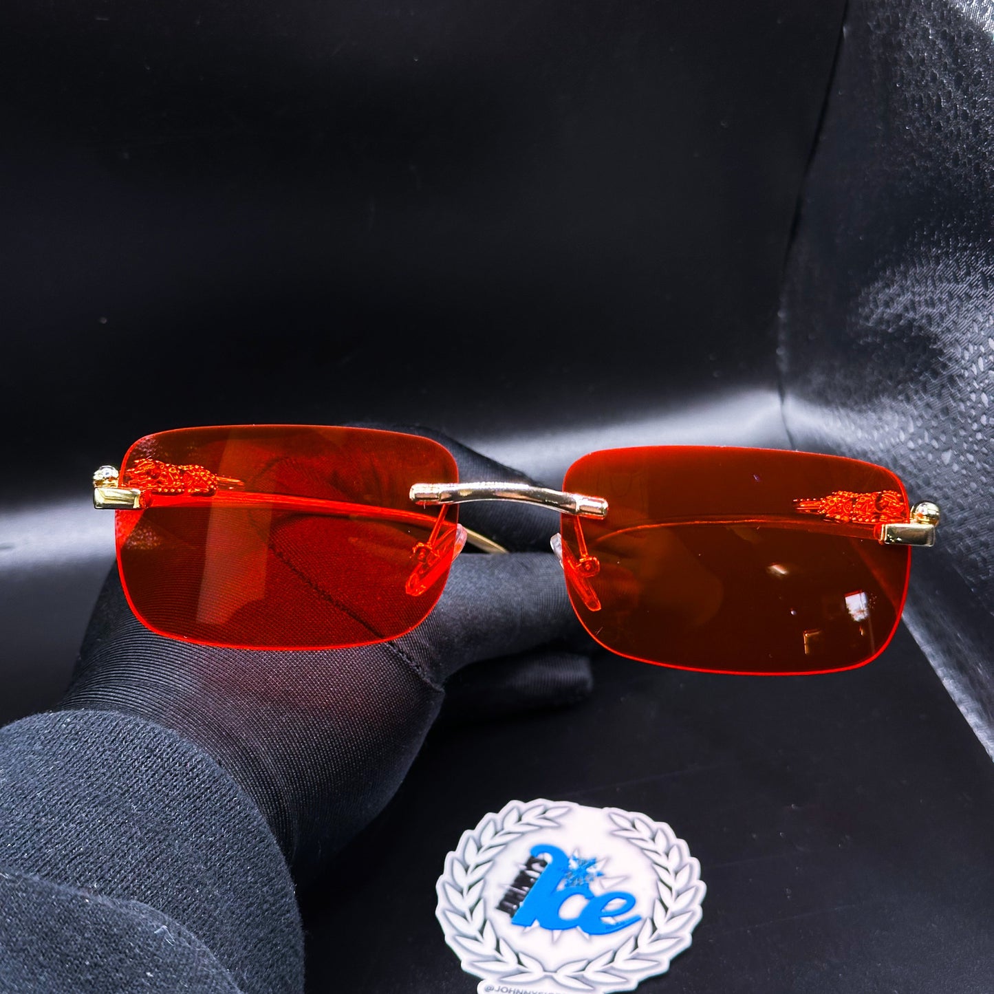 A pair of red tinted sunglasses displayed against a black background with a reflective surface.