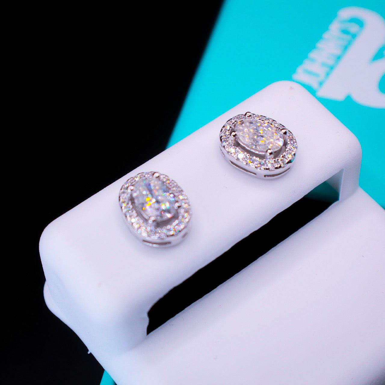 Pair of silver earrings on a white stand with a black and blue background