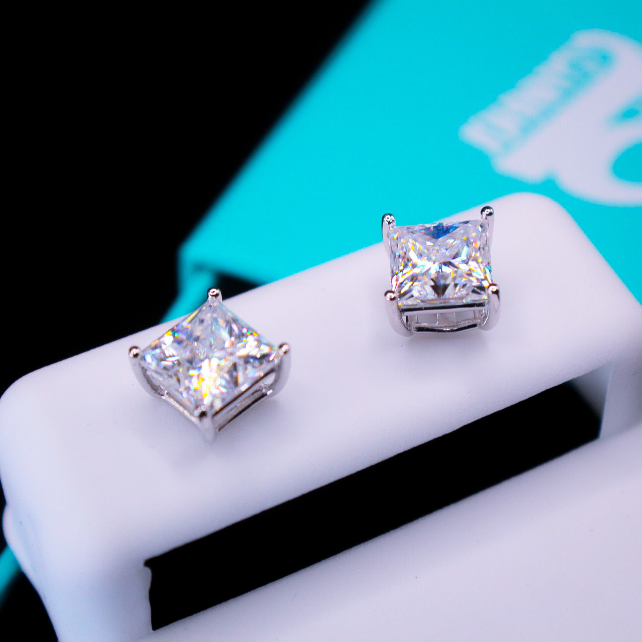 Pair of square-cut stud earrings on a white surface with a blurred background