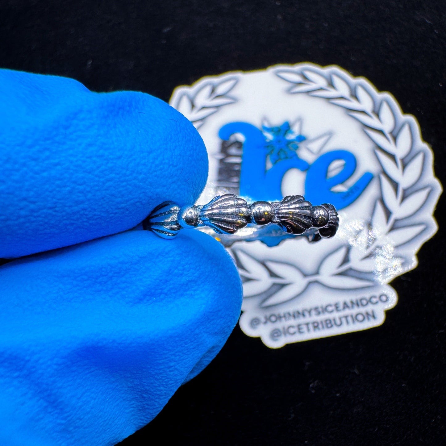 A silver ring with a seashell design, displayed on a blue cloth with a branded white cloth behind it.