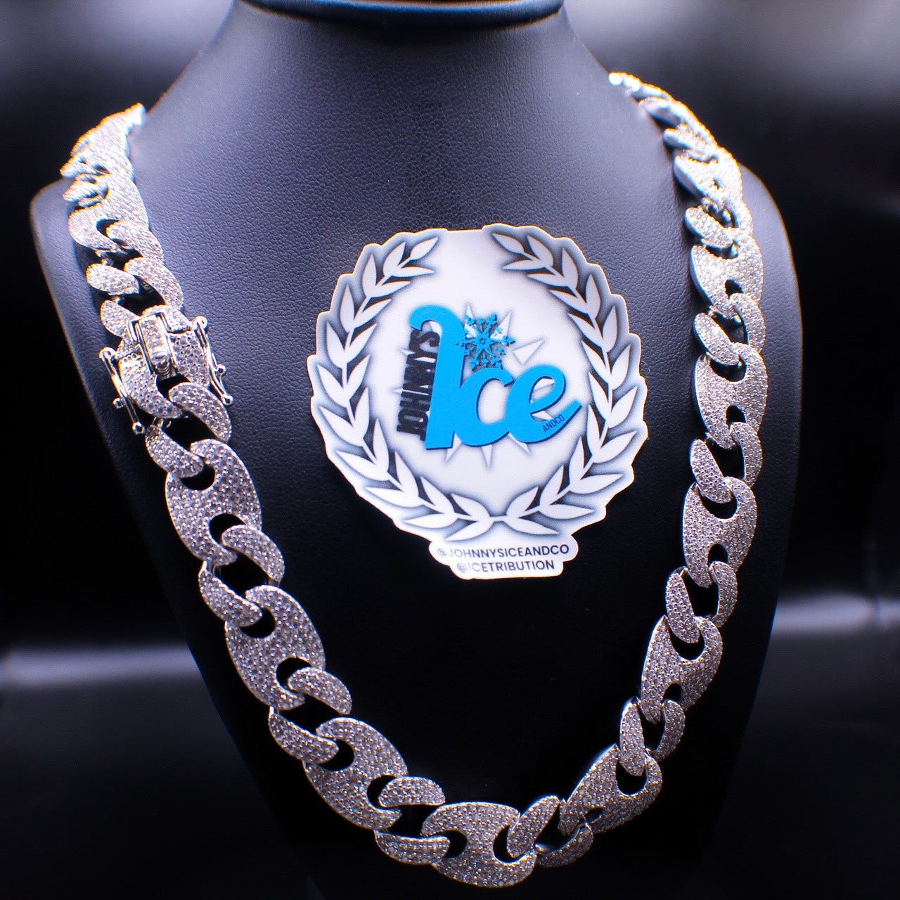 A silver-colored Gucci Bean Chain necklace displayed on a mannequin with a branded plaque in the background.
