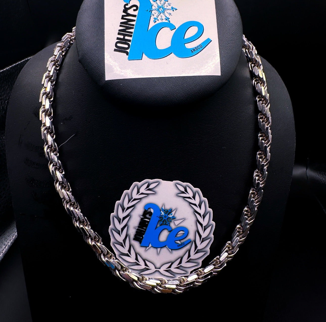 A silver rope chain necklace displayed on a mannequin with a branded display stand in the background.