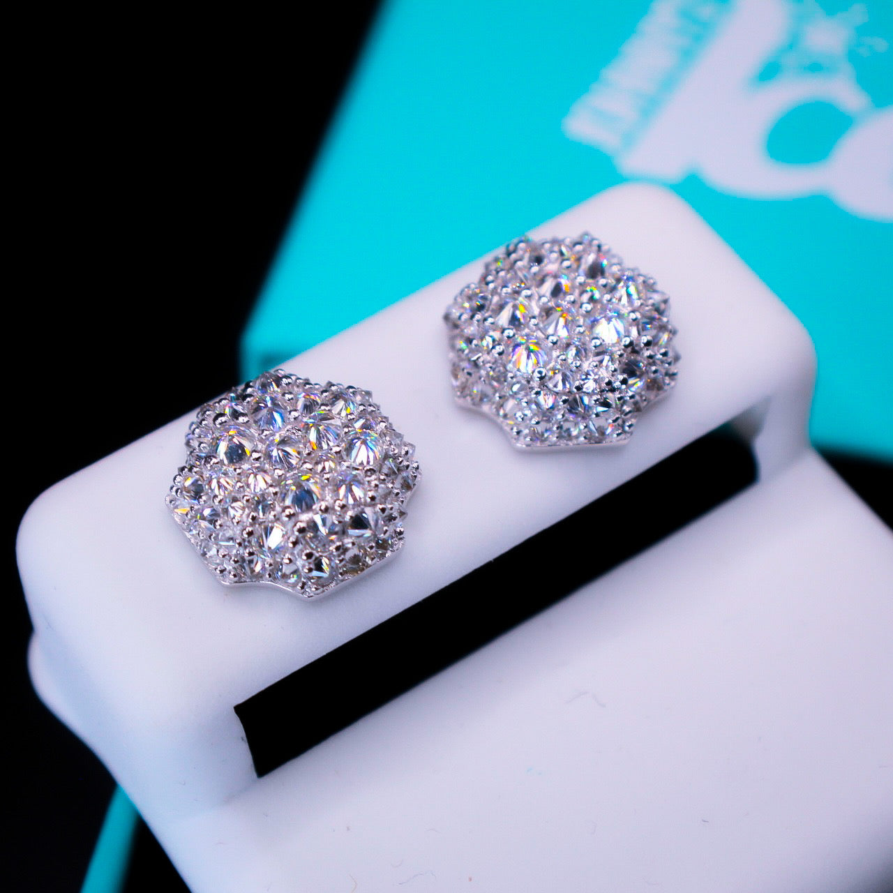 Silver stud earrings on a white stand with a blurred turquoise box in the background