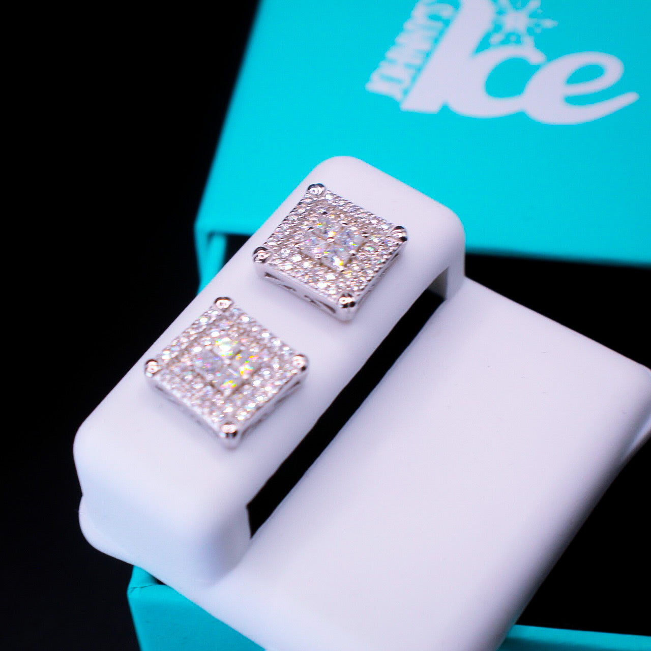 Square-shaped diamond earrings on a white stand with a blue box in the background