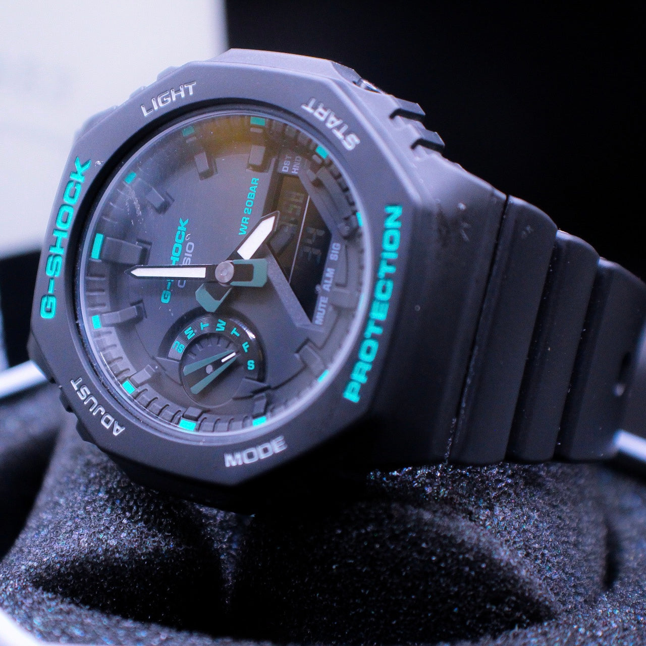 teal and black g shock watch laying on black display 