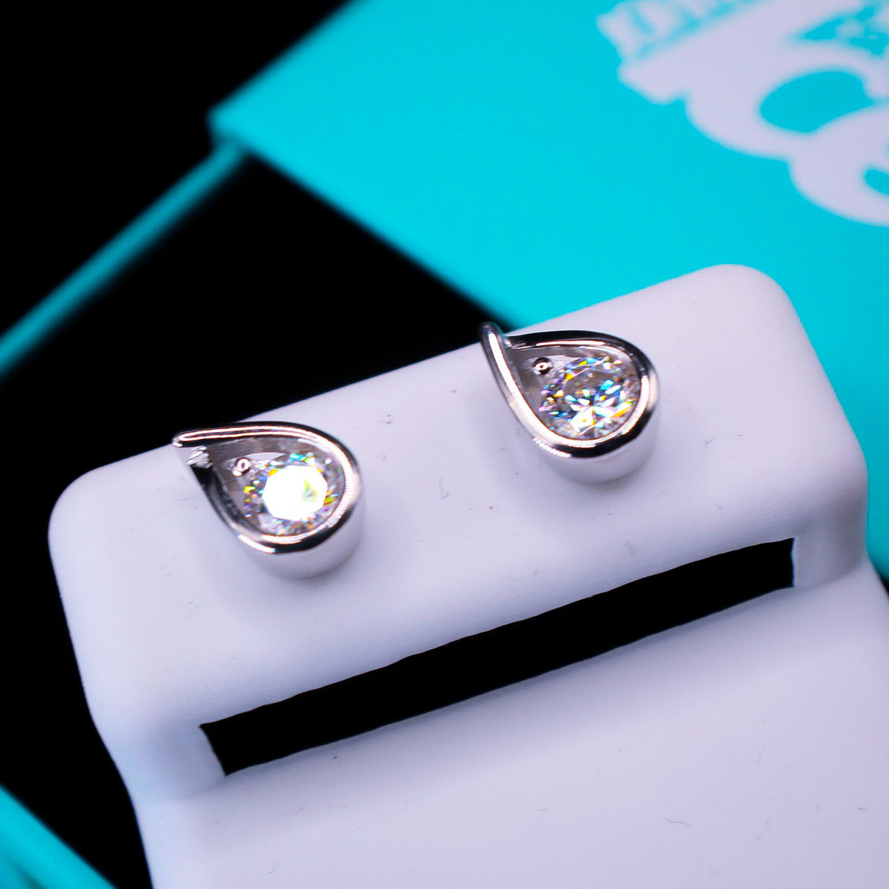 Teardrop-shaped earrings on a white stand with a blurred turquoise background